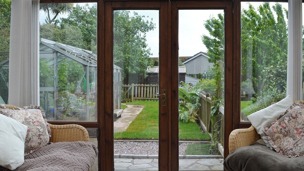Et solarium med glasdør, fletmøbler og udsigt til en have.