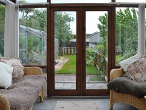 A conservatory with a glass door, wicker furniture, and a view of a garden.