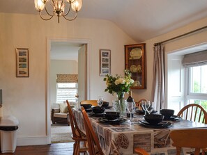 A dining area with a table set for four, a chandelier, and framed pictures on the walls.