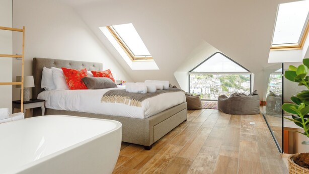 A bedroom with a skylight, a bed with pillows, a bedside table, a sofa, and a view of the city. - 3 bedroom accommodation in Brixham (Brixham)