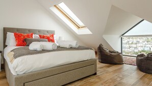 A bedroom with a skylight, a bed with white bedding, and a view of a cityscape through a large window.