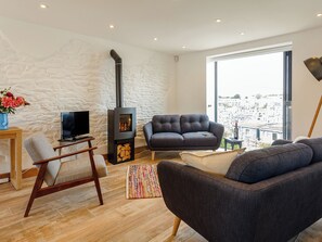 A modern living room with a stone wall, a fireplace, a sofa, a TV, and a view of the city. - 3 bedroom accommodation in Brixham (Brixham)