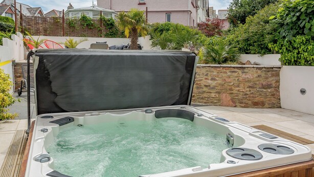 A hot tub with a wooden deck, surrounded by a stone wall and greenery.