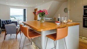 A modern kitchen with a wooden island, bar stools, a vase with flowers, and a view of the sea through a large window. - 3 bedroom accommodation in Brixham (Brixham)