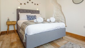 A neatly made bed with a grey headboard, a bedside table with a lamp, and a wall-mounted mirror.