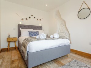 A neatly made bed with a grey headboard, a bedside table with a lamp, and a wall-mounted mirror.