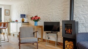 A living room with a stone wall, a television, a fireplace, and a dining area with a vase of flowers. - 3 bedroom accommodation in Brixham (Brixham)