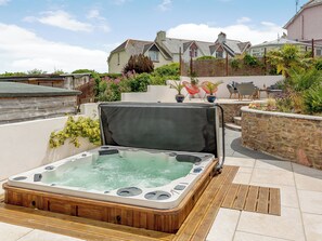 A hot tub on a wooden deck with a stone wall and potted plants in the background. - 3 bedroom accommodation in Brixham (Brixham)