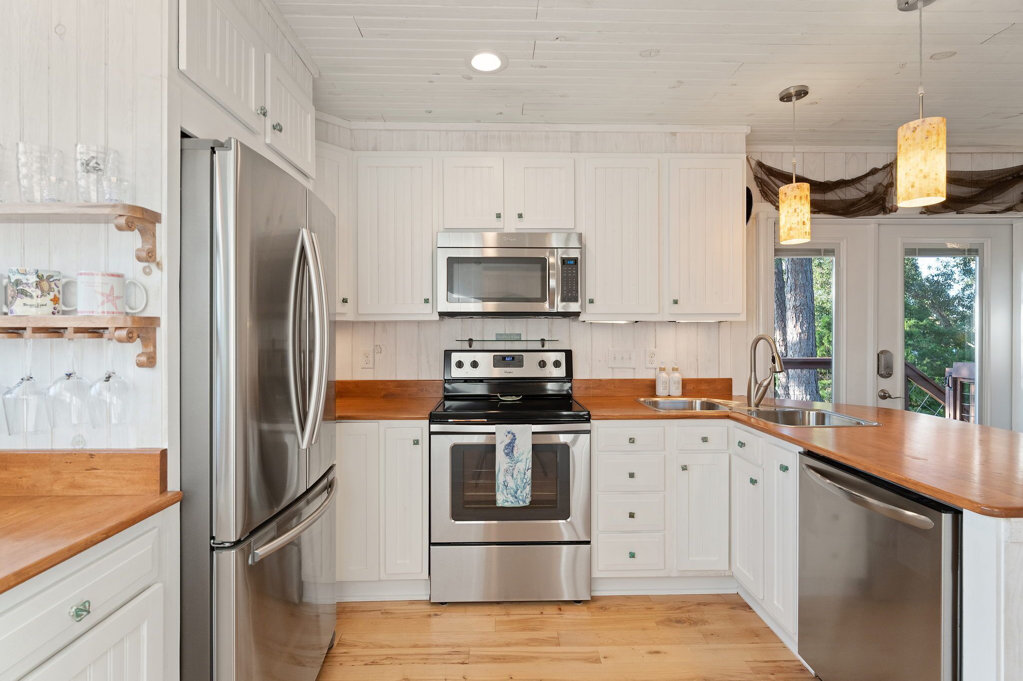 A modern kitchen with stainless steel appliances, white cabinetry, and a wooden countertop.