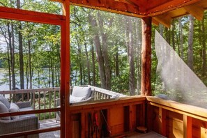 A wooden cabin with a deck overlooking a forested area and a body of water. - Amazingly comfortable and secluded Northwoods getaway (Hayward)