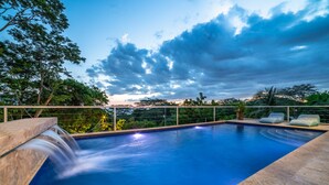Piscina com cachoeira, rodeada por um deck de madeira e espreguiçadeiras.