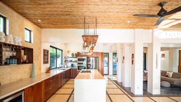 Uma cozinha moderna com ilha central, teto de madeira e espaço bar com copos e garrafas.