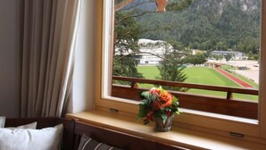 A room with a large window overlooking a mountainous landscape, a wooden desk, and a vase with flowers. - Ferienwohnung für 2 Personen mit großem Balkon, 79 m² (Inzell)