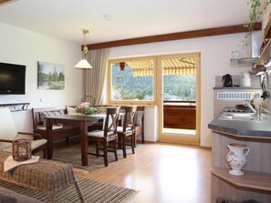 Un coin repas accueillant avec une table et des chaises en bois, un téléviseur fixé au mur et une fenêtre donnant sur un paysage verdoyant.