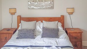 A neatly made bed with a striped bedspread, two patterned pillows, and a wooden headboard. There are two bedside tables with lamps and a wall-mounted abstract painting above the bed. - 4 bedroom accommodation in Keswick (Keswick)