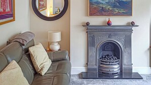 A living room with a grey sofa, a round mirror, a painting, a fireplace, and a lamp. - 4 bedroom accommodation in Keswick (Keswick)