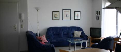A living room with a blue sofa, a glass coffee table, a wooden dining table, and a television.