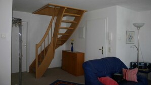 Et værelse med en trætrappe, en blå sofa, et lille skab og en gulvlampe.