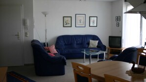 En stue med en blå sofa, et glasbord, et træspisebord og et fjernsyn.