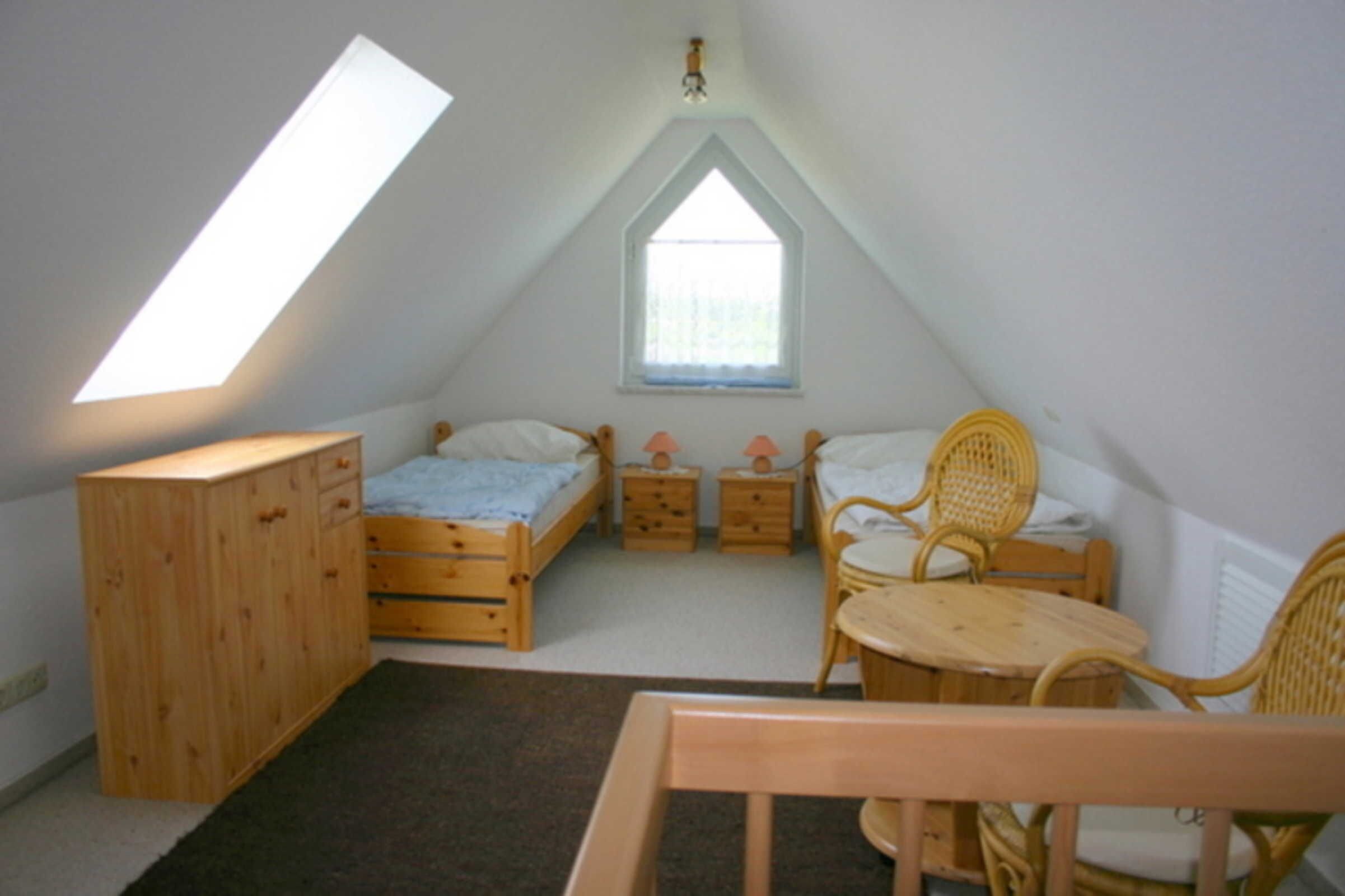 A bedroom with a sloped ceiling, a window, a bed, a dresser, a chair, and a small table.