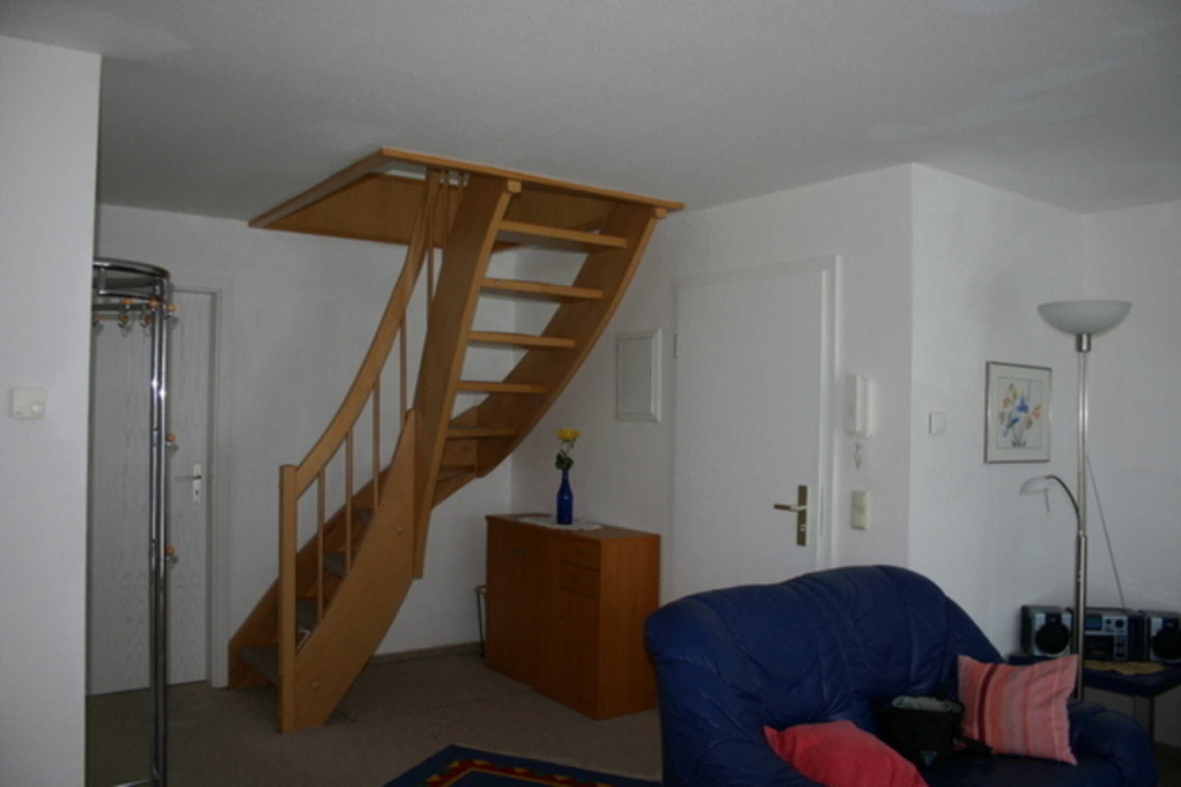 Ein Zimmer mit einer Holztreppe, einem blauen Sofa, einem kleinen Schrank und einer Stehlampe.