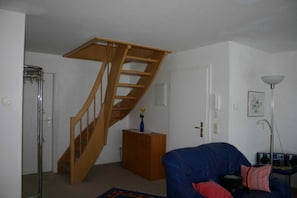 Une pièce avec un escalier en bois, un canapé bleu, un petit meuble et un lampadaire.