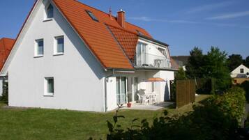 Ein zweistöckiges Haus mit Schrägdach, einem Balkon und einem kleinen Garten.