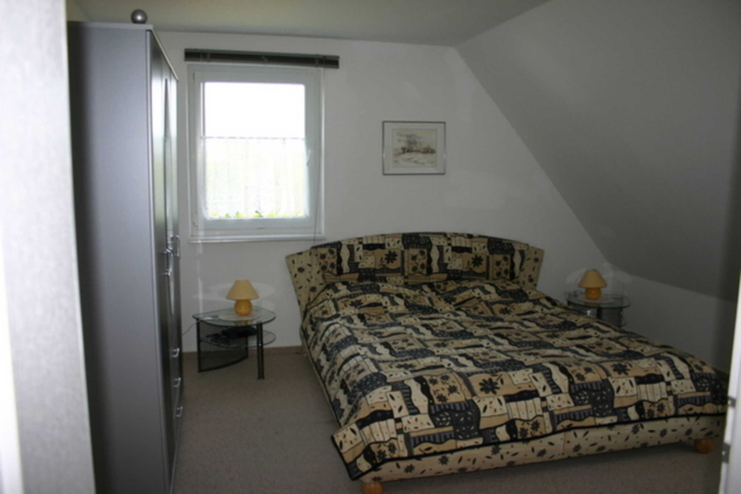 A bedroom with a bed, a window, a small table with a lamp, and a picture on the wall.
