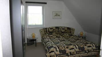 A bedroom with a bed, a window, a small table with a lamp, and a picture on the wall.