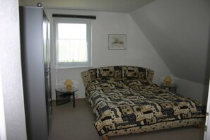 Une chambre à coucher avec un lit, une fenêtre, une petite table avec une lampe et un tableau au mur.