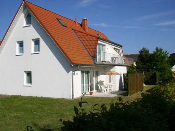Een twee verdiepingen tellend huis met een rood dak, een balkon en een klein terras.