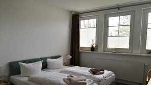 Une chambre d’hôtel avec deux lits, une fenêtre avec des stores, une table de chevet avec une lampe et un radiateur.