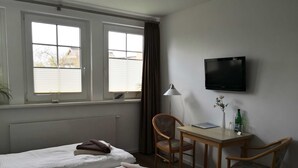 Une chambre d’hôtel avec deux lits, un bureau avec une chaise, une télévision et une fenêtre avec des stores.