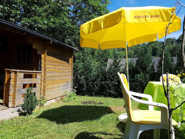 A wooden cabin with a yellow umbrella, a white plastic chair, and a small table.