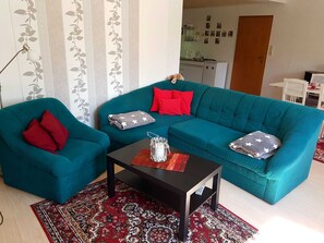 A teal sofa with red and gray pillows, a small table with a remote, and a patterned rug.