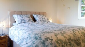 Une chambre à coucher avec un lit, une table de chevet, une lampe et une fenêtre avec des rideaux.