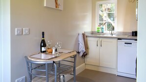 Une cuisine avec une table à manger, des chaises, une bouteille de vin, des verres, une fenêtre et un lave-vaisselle.