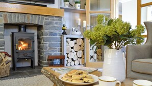 A cozy living room with a stone fireplace, a television mounted above it, and a comfortable seating area with a sofa and armchairs. - Maes Y Bryn Farmhouse (Llansadwrn, near Llandeilo)