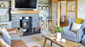 A living room with a stone fireplace, a television, a sofa, a coffee table, and a door leading to another room. - Maes Y Bryn Farmhouse (Llansadwrn, near Llandeilo)