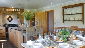 A kitchen with wooden cabinets, a dining table set with white plates, glasses, and a variety of food items. - Maes Y Bryn Farmhouse (Llansadwrn, near Llandeilo)