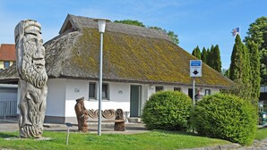 A traditional building with a thatched roof, a stone sculpture, and a sign indicating a parking area.