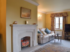 Una sala de estar con chimenea, un sofá, un televisor y una ventana con cortinas.
