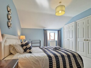 Een slaapkamer met een bed, een bedlamp, gordijnen, een radiator en een kledingkast.