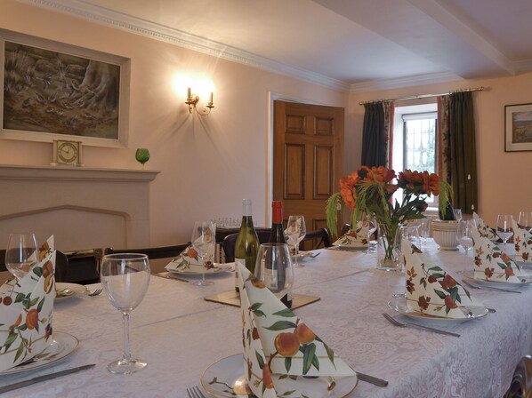 Une salle à manger avec une longue table dressée pour le repas, un tableau accroché au mur et une fenêtre ornée de rideaux.