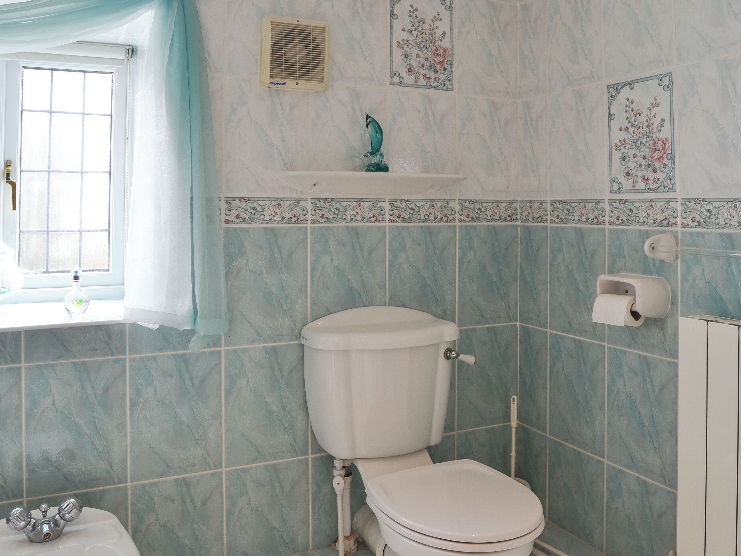 Een badkamer met toilet, een raam met gordijn, douche en wastafel.