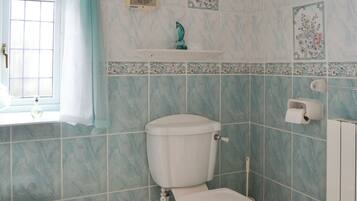 Een badkamer met toilet, een raam met gordijn, douche en wastafel.