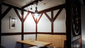Una habitación acogedora con vigas de madera a la vista, un banco de madera, una mesa con una jarra de vidrio y una lámpara colgante.