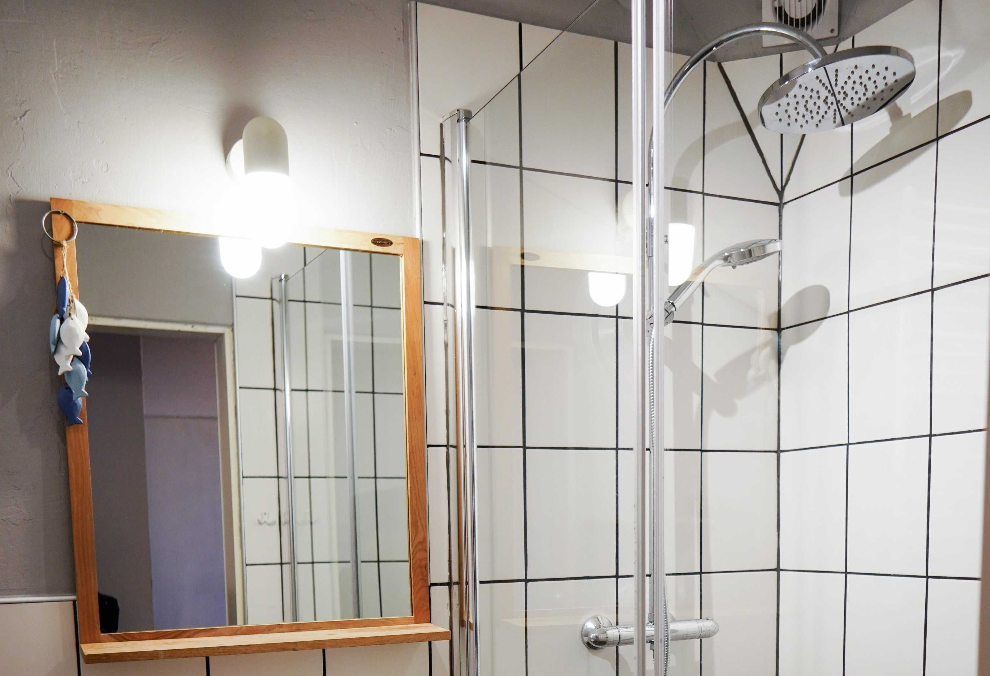 Ein Badezimmer mit einer Duschkabine aus Glas, einem spiegel mit Holzrahmen und gefliesten Wänden.