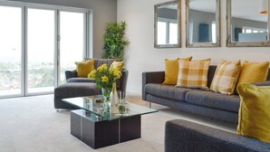 A modern living room with a glass coffee table, grey sofas, yellow cushions, and large mirrors on the wall. - 3 bedroom accommodation in Prestatyn (Prestatyn)