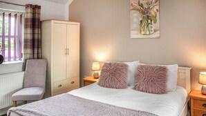 A bedroom with a bed, a chair, a wardrobe, and a bedside table with a lamp. - Bullions Farm Cottage (Consett)